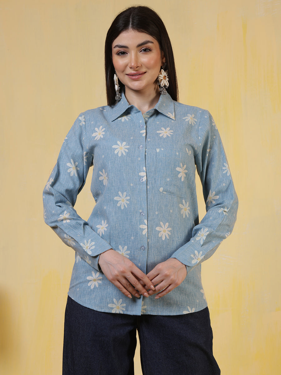 Women’s blue denim-look shirt with white floral print, long sleeves, button-down front, and collared neckline, paired with dark jeans