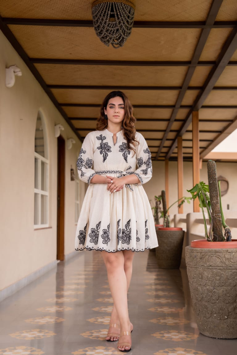 Woman wearing an ivory short flared dress with black floral embroidery, 3/4th sleeves, and a keyhole neckline.