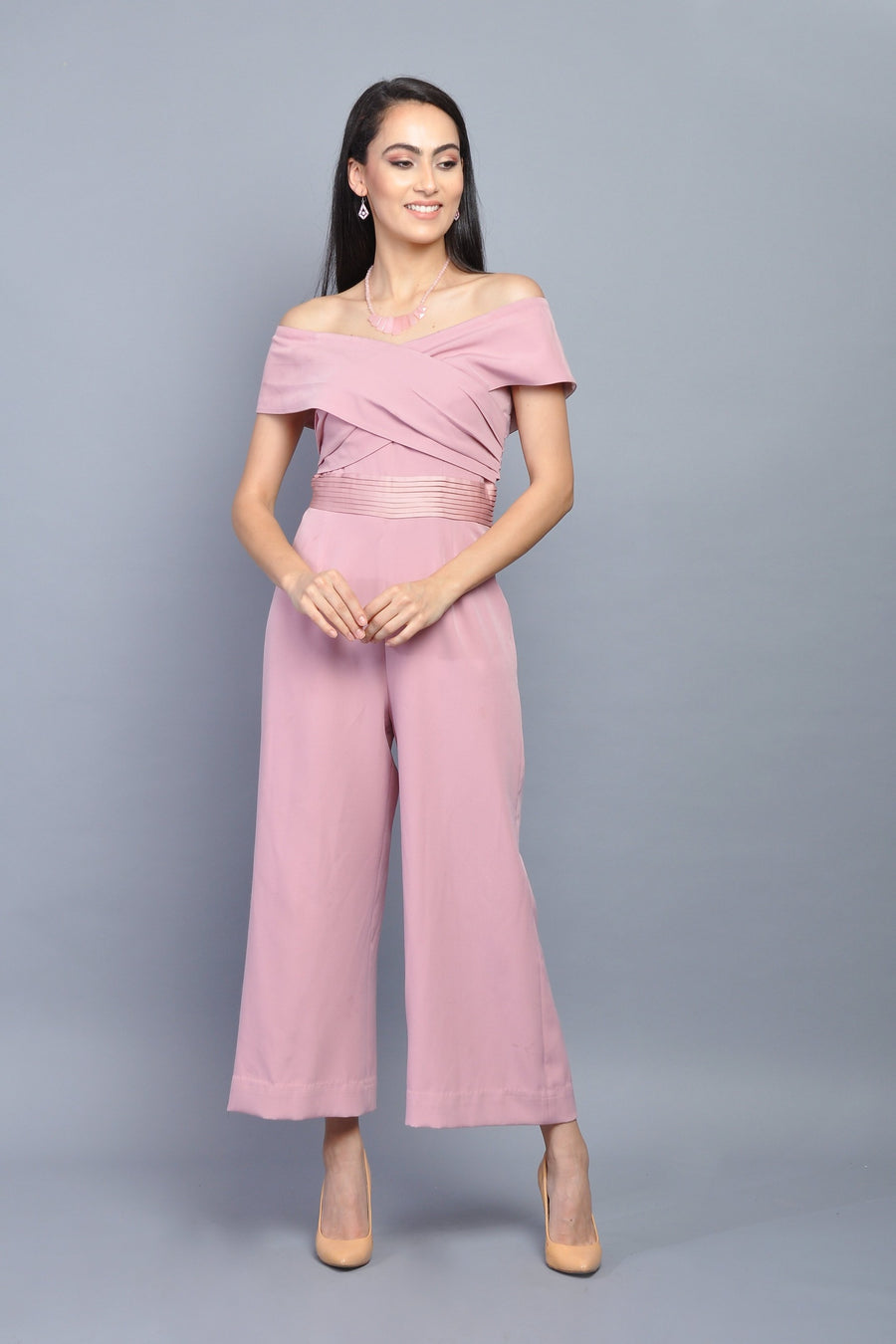 Woman wearing an elegant off-shoulder dusty pink wide-leg jumpsuit with pleated waist detailing.