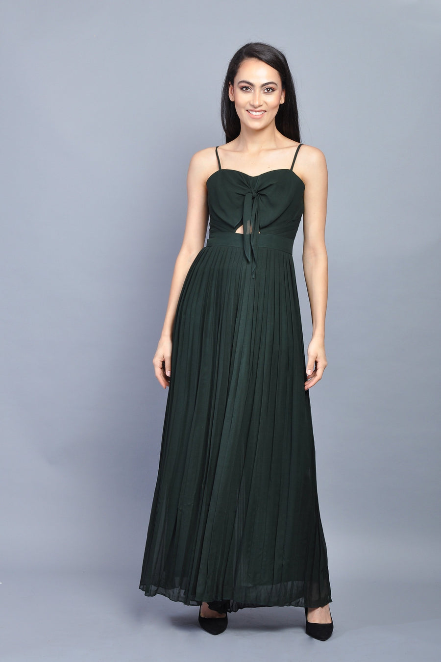 Woman wearing a dark green pleated maxi dress with spaghetti straps and front knot detail.
